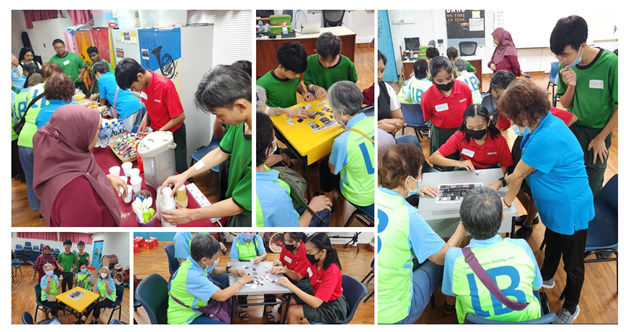 Groups of people in green and blue vests participate in indoor activities at tables during a community event.